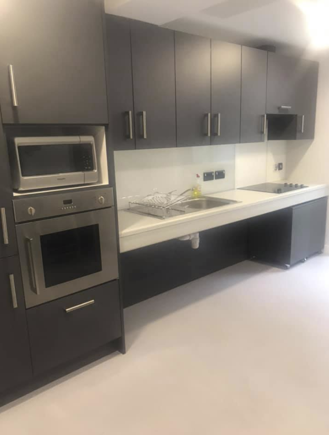Student accommodation kitchen with oven, microwave, stove, sink, and cupboards